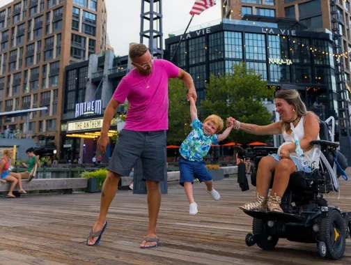 Parents hold their child's hands and swing him in the air as they enjoy a day on the Wharf. 